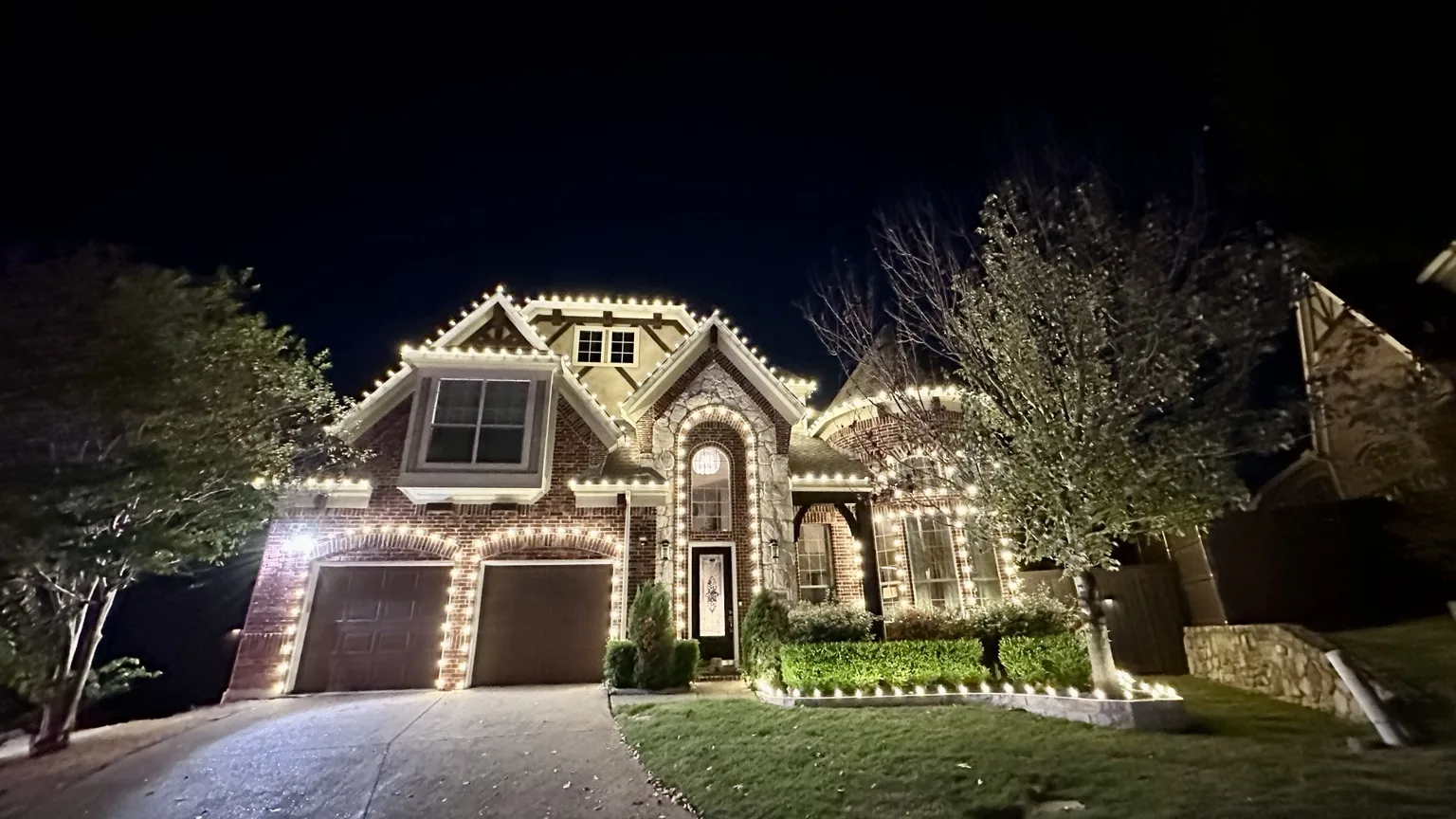 Warm white Christmas light installation across rooflines, windows, wreaths and illuminated reindeer