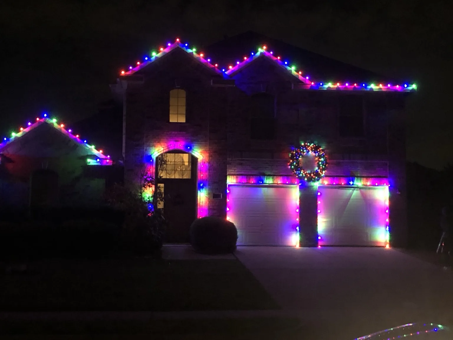 Warm white Christmas lights outlining a large home with illuminated reindeer in the yard