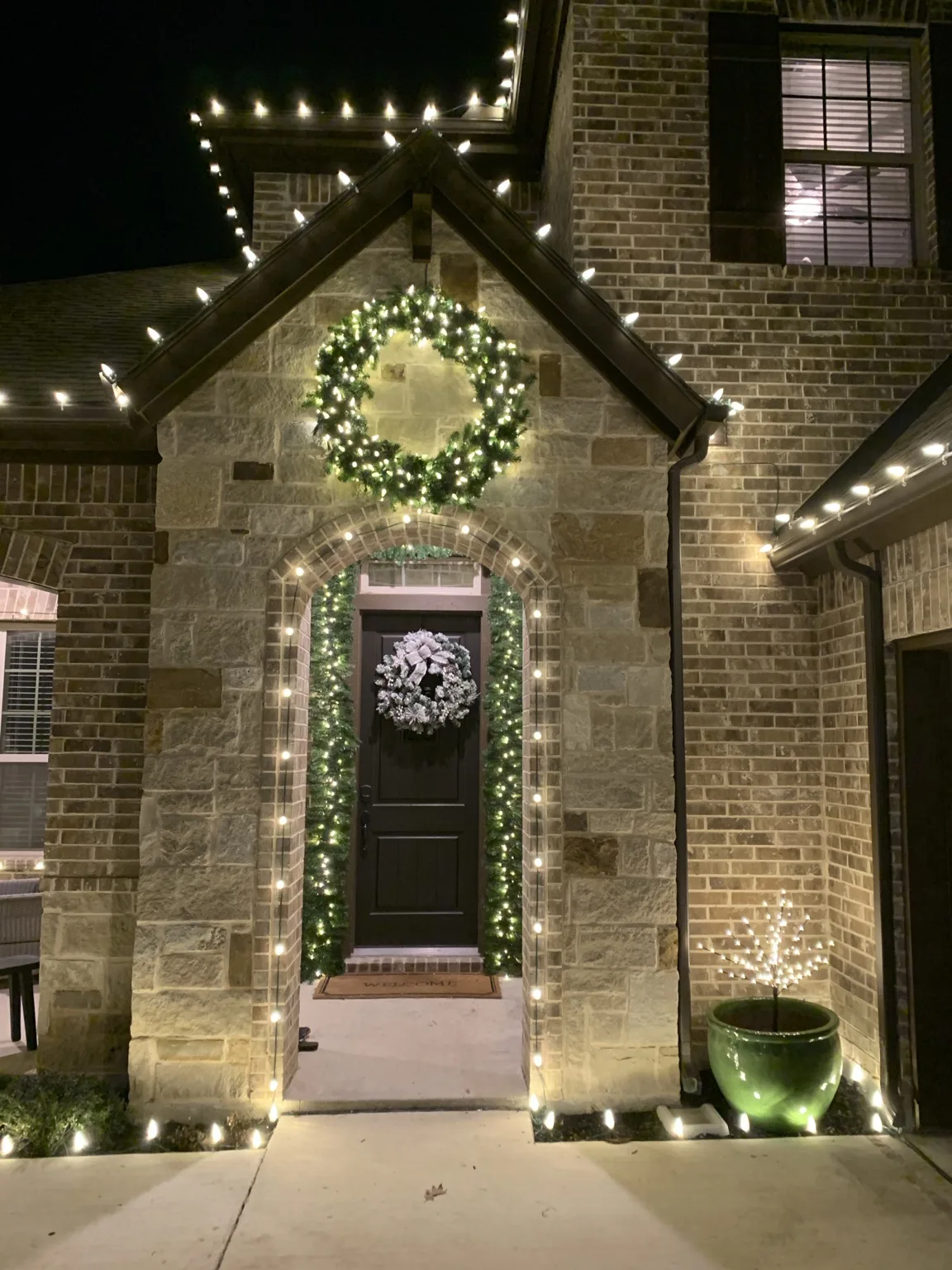 Warm white Christmas lights framing a stone entry arch with wreath and garland